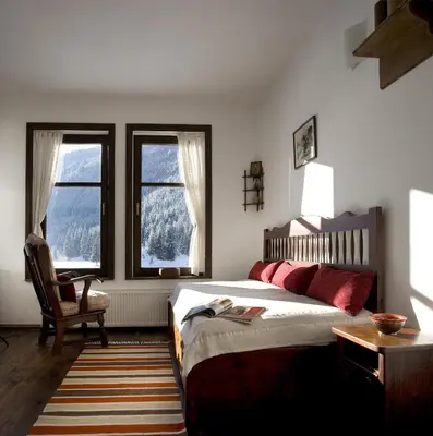 a bedroom with a bed and a chair and two windows at Family Hotel Arkan Han in Trigrad