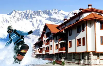 a person riding a snowboard in front of a building at Pirin River Ski, Fun and Family in Bansko