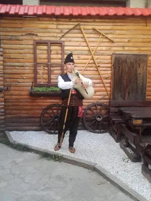 a man playing a instrument in front of a wooden cabin at Guesthouse Vazrozhdenski kashti in Manastir
