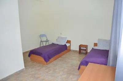 a bedroom with two beds with purple sheets and a chair at Семеен хотел Пауталия in Kyustendil