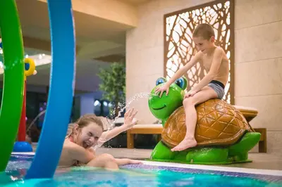 a young child riding on a turtle in a pool at Park & Spa Hotel Markovo in Plovdiv