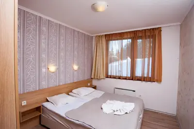 a bedroom with a bed with white sheets and a window at Forest Nook Aparthotel in Pamporovo
