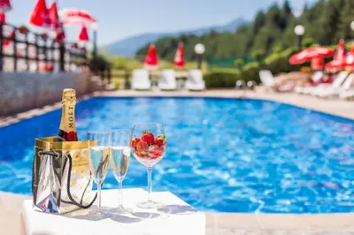 two glasses of wine and a bottle of champagne next to a swimming pool at Spa Hotel Aspa Vila in Banya