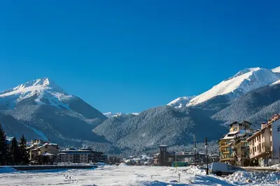 a town with snow covered mountains in the background at PIRIN PLACE Bansko in Bansko
