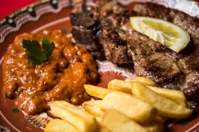 a plate of food with meat and chips on a table at Banskovilla Zlateva House in Bansko