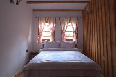 a bedroom with a bed with white sheets and two windows at ЧОЛАКОВАТА КЪЩА in Koprivshtitsa