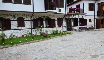 a courtyard of a building with a bench and flowers at Family Hotel Dinchova kushta in Rozhen