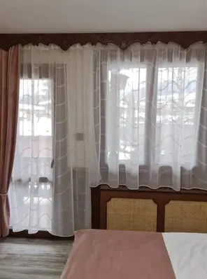 a bedroom with a bed and a window with white curtains at Chuchura Family Hotel in Koprivshtitsa