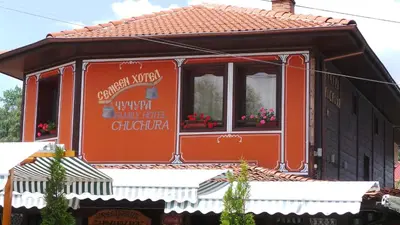 an orange house with flowers in the window at Chuchura Family Hotel in Koprivshtitsa