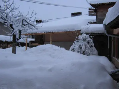 a yard covered in snow with a house at Guest Rooms Bashtina Striaha in Koprivshtitsa