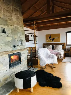 a living room with a stone fireplace and a bed at Rodope Nook Guest house in Chepelare