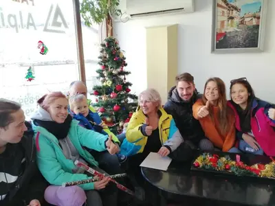 a group of people sitting around a table in front of a christmas tree at Hotel Alpin - 91 Bansko in Bansko
