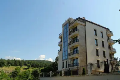 a tall white building with a fence around it at Garden Guest House in Sandanski