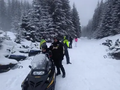 a group of people standing in the snow with a snowmobile at Ski Chalets at Pamporovo - an affordable village holiday for families or groups in Pamporovo