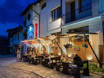 a group of people sitting at tables outside of a building at Family House Oreha in Bansko