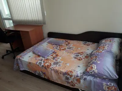 a bed with a flowered comforter with a table and a desk at Guest House Mania in Sofia