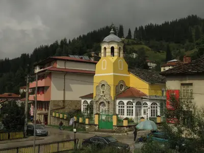 a yellow building with a clock tower in a town at Willy Villy's Home- Chepelare in Chepelare