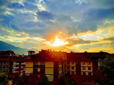 a building with the sun setting in the background at Casual Apartment near Gondola & City Center - Neon in Bansko