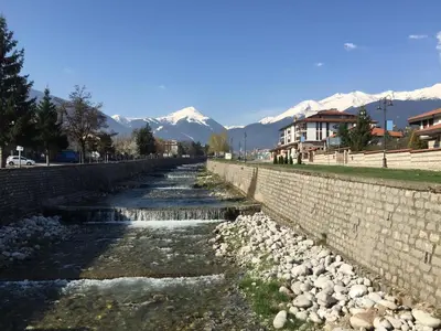 a river with a stone wall and mountains in the background at ★ Chic & Elegant 1 Bedroom in Eagle's Nest Complex ★ Close to Gondola and Bar Street in Bansko
