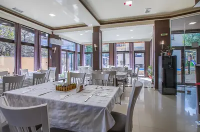 a dining room with a table and chairs and windows at Family Hotel Zornitsa in Ribarica