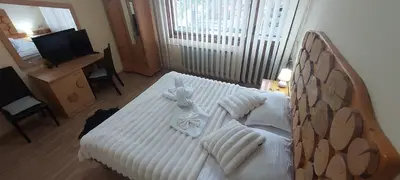 a bedroom with a white bed with a wooden headboard at Guest House Planinski Zdravets in Bansko