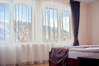a bedroom with two beds and two large windows at СТАИ ЗА ГОСТИ в КЪЩА КАМЕЛИЯ in Pamporovo