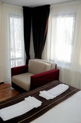 a room with a bed and a chair and window at СТАИ ЗА ГОСТИ в КЪЩА КАМЕЛИЯ in Pamporovo