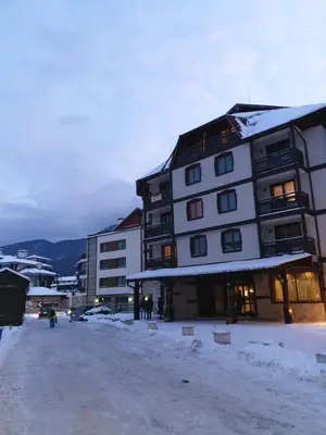 a building with snow on the ground next to some buildings at Simonen Apartments near the Gondola in Bansko