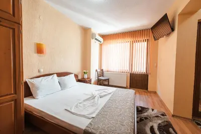 a bedroom with a bed with white sheets and a window at Семеен хотел Свети Георги in Sandanski