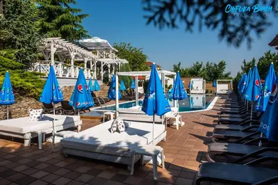 a pool with blue umbrellas and tables and chairs at Chiflika Family Hotel in Asenovgrad
