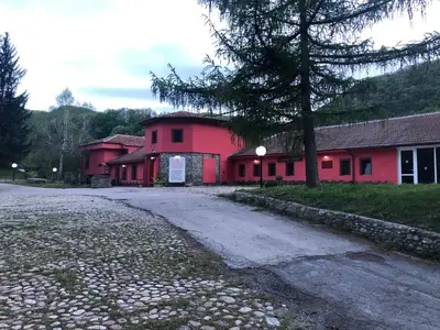 a red building with a tree next to a street at Zlatna ribka in Kokolyane