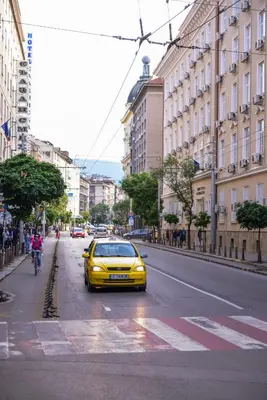 a yellow car is driving down a city street at MOCCA Studio next to Crystal Garden and Russian Church by Flat Mаnager in Sofia