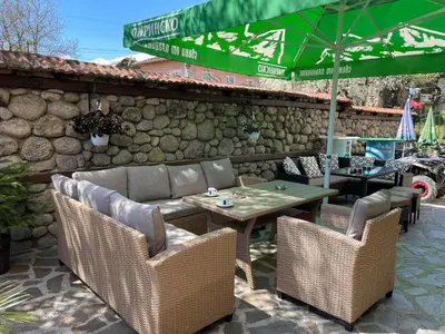 a patio with a table and chairs and a green umbrella at Къща за гости Александра in Dobrinishte