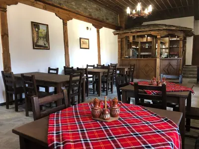 a restaurant with wooden tables and chairs in a room at Пачаловата къща in Kovachevitsa