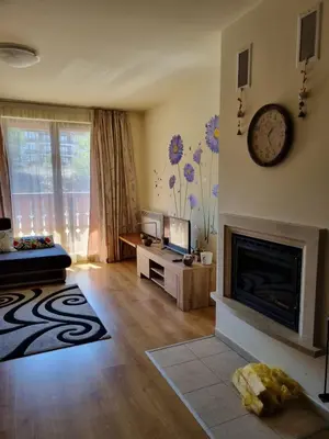 a living room with a fireplace and a clock on the wall at G-Apartment, New Inn, 2-rooms in Bansko