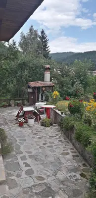 a stone patio with a table and a tower in a garden at Mechta Guest House in Koprivshtitsa