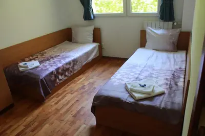 two beds in a room with wooden floors and two windows at Апартаменти Уют in Plovdiv