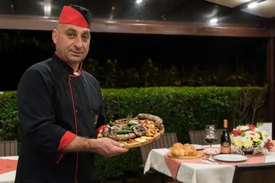 a man holding a plate of food in front of a table at Zlaten Rozhen Family Hotel- Monument of Cultural Significance in Rozhen