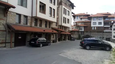 two cars parked on a street next to buildings at Apartman u kompleksu Royal Towers in Bansko