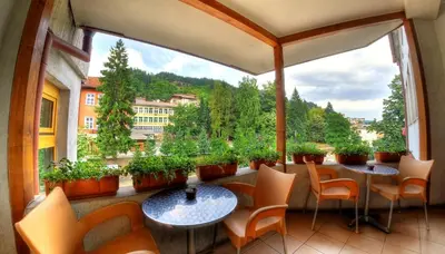 a balcony with tables and chairs and a large window at Plaza Family Hotel in Smolyan