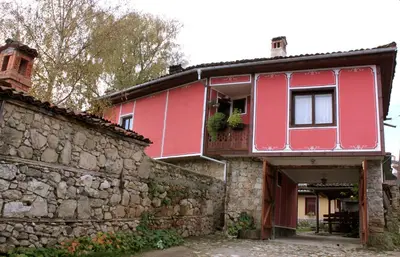 a red house next to a stone wall at Nenchova Guest House in Koprivshtitsa