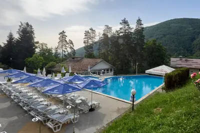 a swimming pool with chairs and blue umbrellas at Constantzia Balneohotel in Kostenets Village