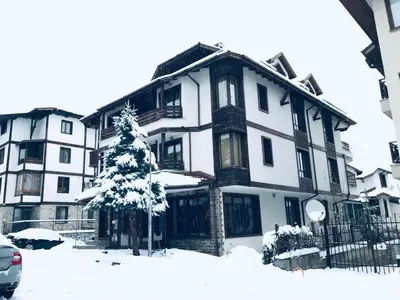 a snow covered building with a tree in front of it at Guest House ANEX in Bansko