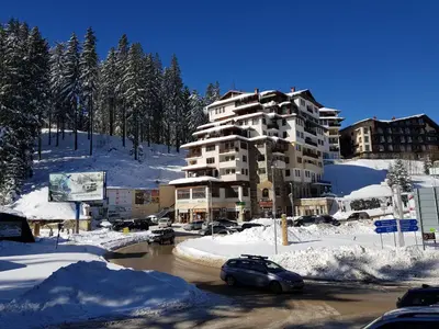 a large apartment building in the snow with cars parked at Апартамент Pamporovo Palace in Pamporovo