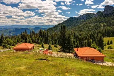 two buildings on a grassy hill with mountains in the background at Вила Морава in Pamporovo