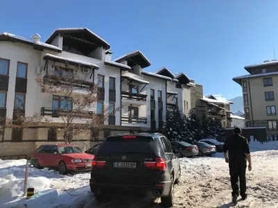 a man walking past a car parked in the snow at Dolomiti Apartments in Bansko