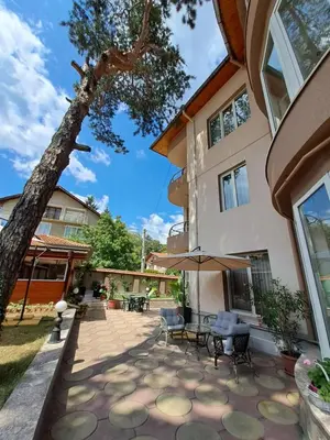 a patio with tables and chairs and a tree at Приятелската къща in Velingrad
