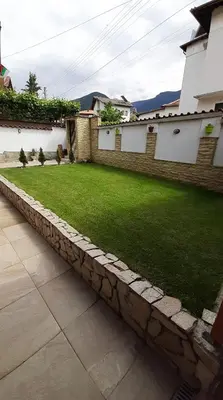 a garden with a stone retaining wall and a lawn at Къща за гости Чечев in Sapareva Banya