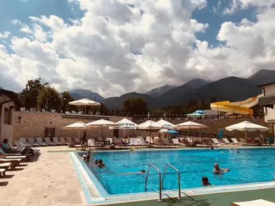 a pool with people swimming in it with mountains in the background at Luxury Downtown Apartment - Gondola in Bansko