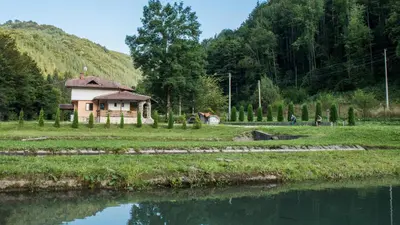 a small house in a field next to a body of water at Къща за гости Черна река in Ribarica